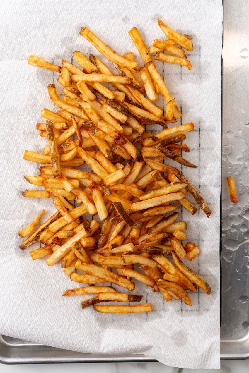 homemade french fries draining on a paper towel lined wire rack