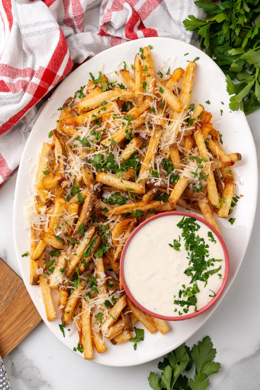 Parmesan truffle fries with garlic aioli sprinkled with fresh chopped herbs on a white platter