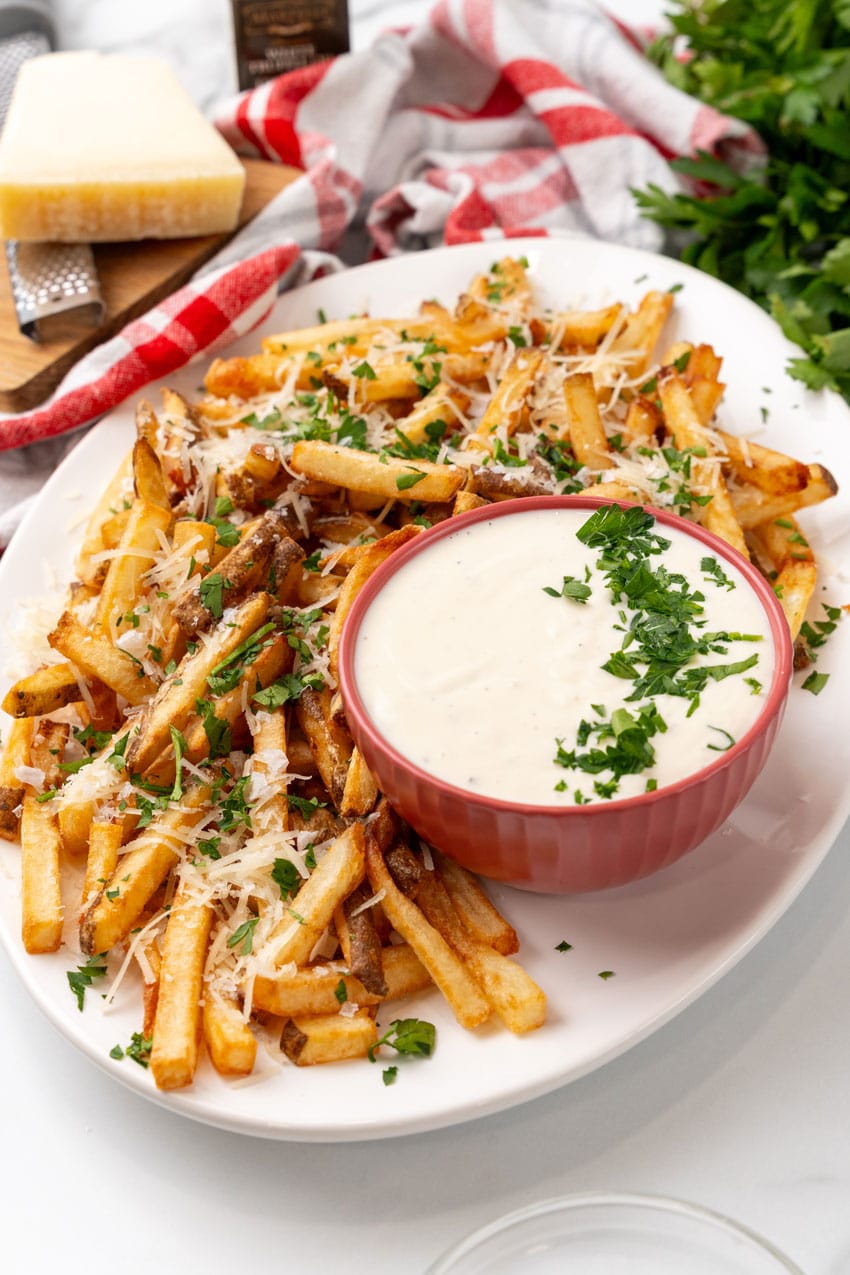 Parmesan truffle fries with garlic aioli sprinkled with fresh chopped herbs on a white platter