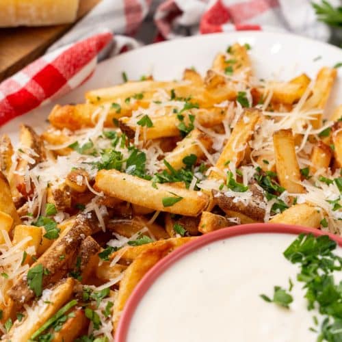 Parmesan truffle fries with garlic aioli sprinkled with fresh chopped herbs on a white platter