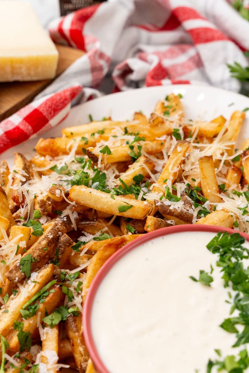 Parmesan truffle fries with garlic aioli sprinkled with fresh chopped herbs on a white platter