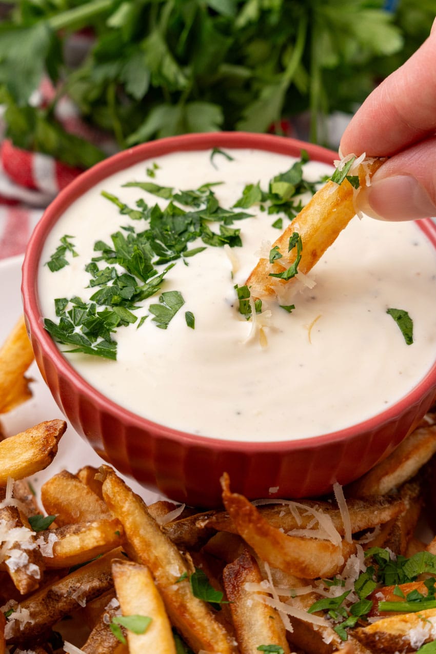 a homemade french fry being dipped into a small bowl filled with garlic aioli