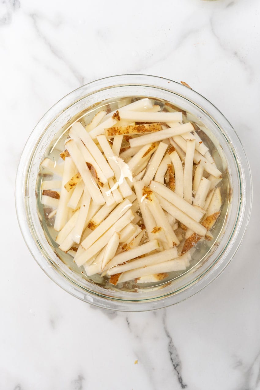 fresh cut fries soaking in salted water in a glass mixing bowl