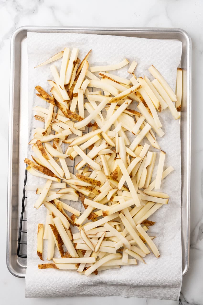 fresh cut fries draining on a paper towel lined wire rack