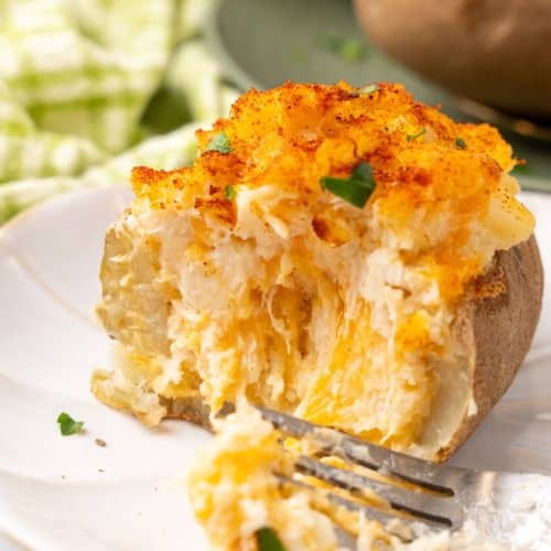 twice baked crab stuffed potato on a small white plate with a silver fork resting on the side