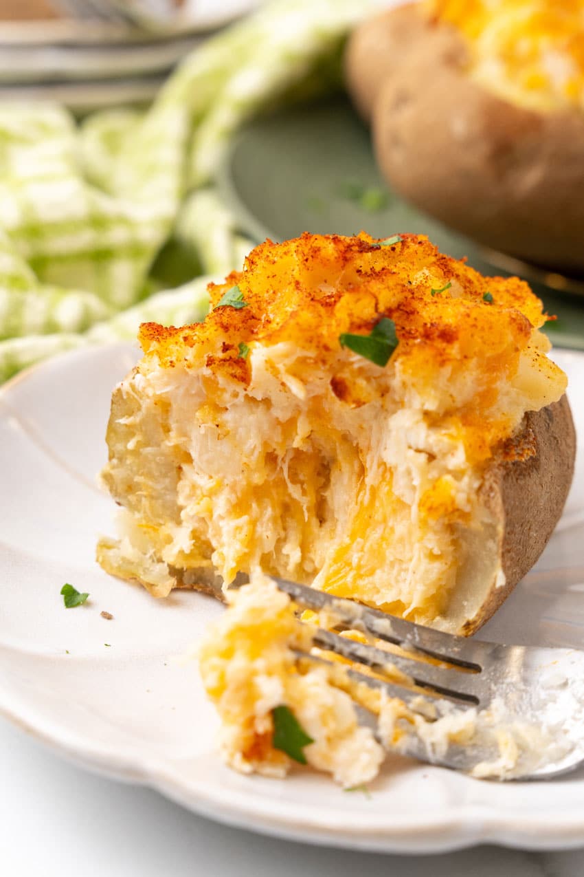 twice baked crab stuffed potato on a small white plate with a silver fork resting on the side