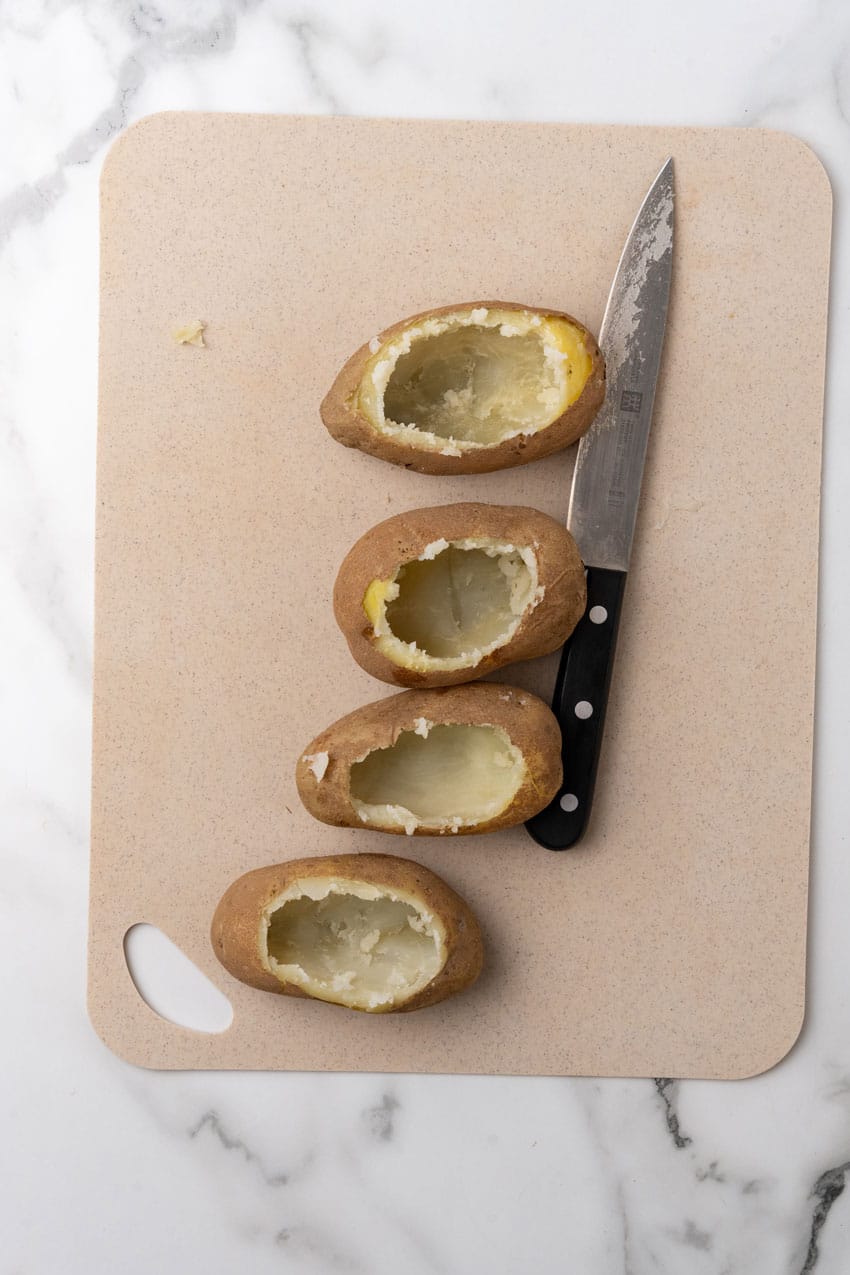 hollowed out baked potatoes on a plastic cutting board