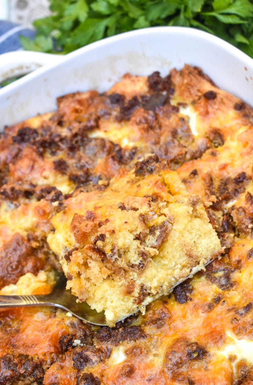 a silver spatula lifting a slice of cheddar bay breakfast bake out of a white casserole dish