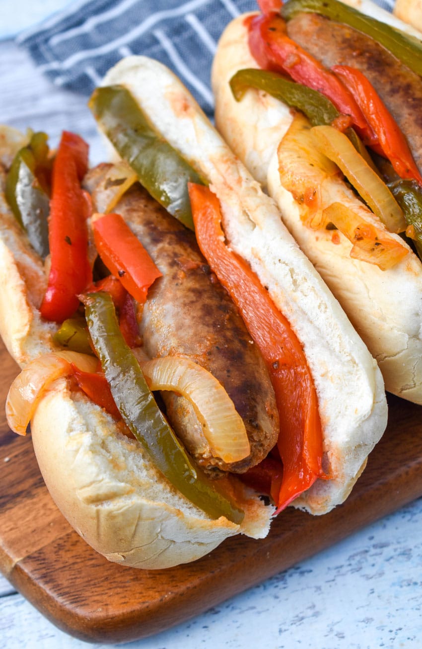 slow cooker sausage with peppers and onions in soft fluffy buns arranged in a row on a wooden cutting board