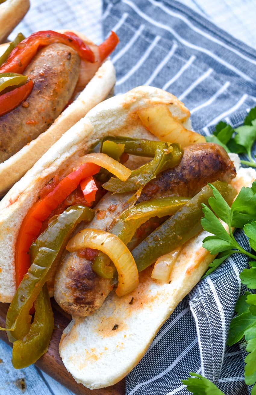 slow cooker sausage with peppers and onions in soft fluffy buns arranged in a row on a wooden cutting board