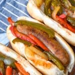 slow cooker sausage with peppers and onions in soft fluffy buns arranged in a row on a wooden cutting board