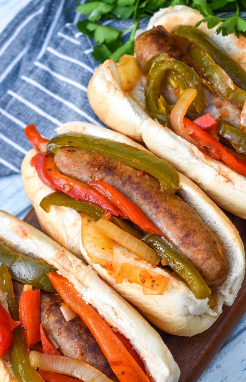 slow cooker sausage with peppers and onions in soft fluffy buns arranged in a row on a wooden cutting board