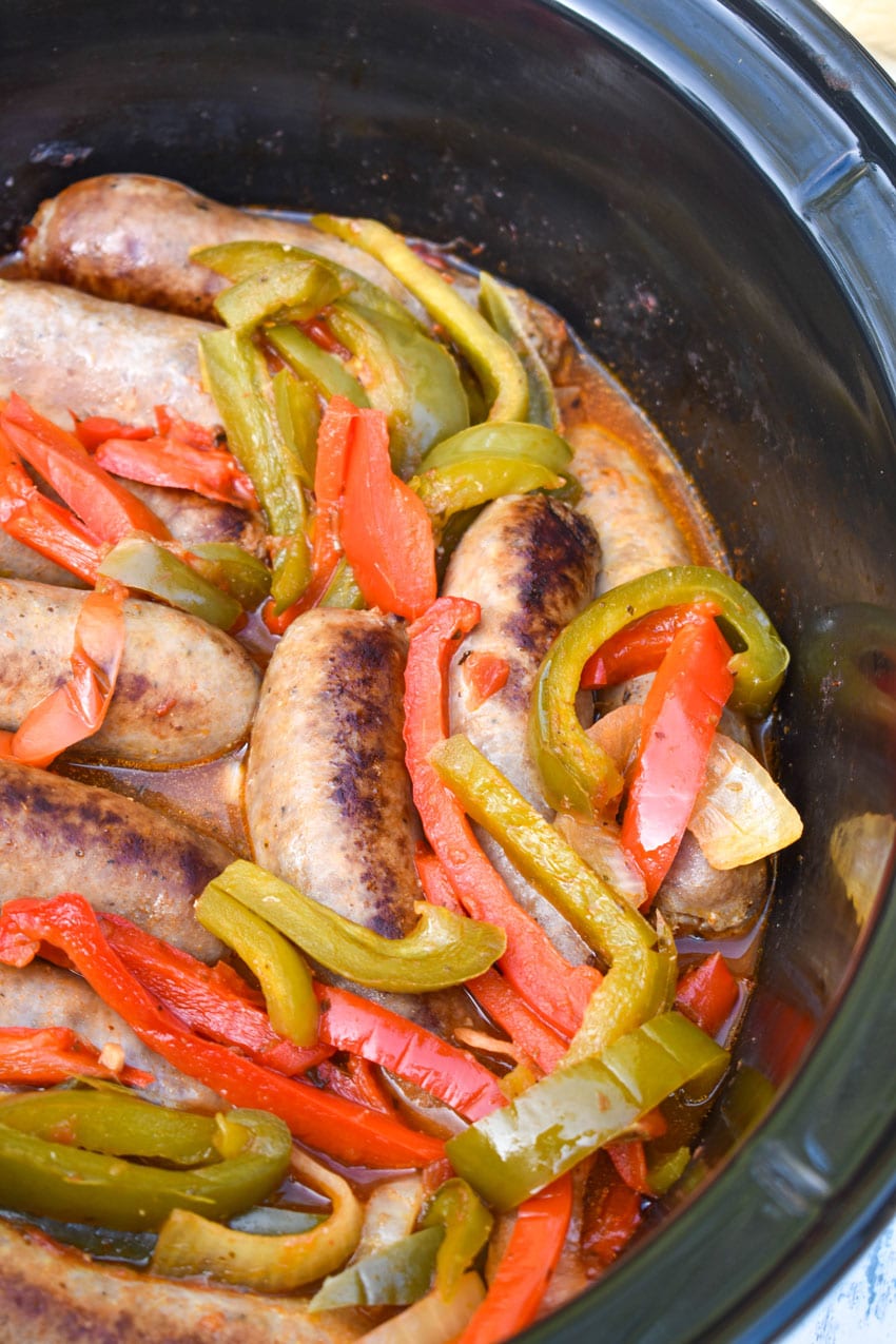 slow cooker sausage with peppers and onions in a black crock