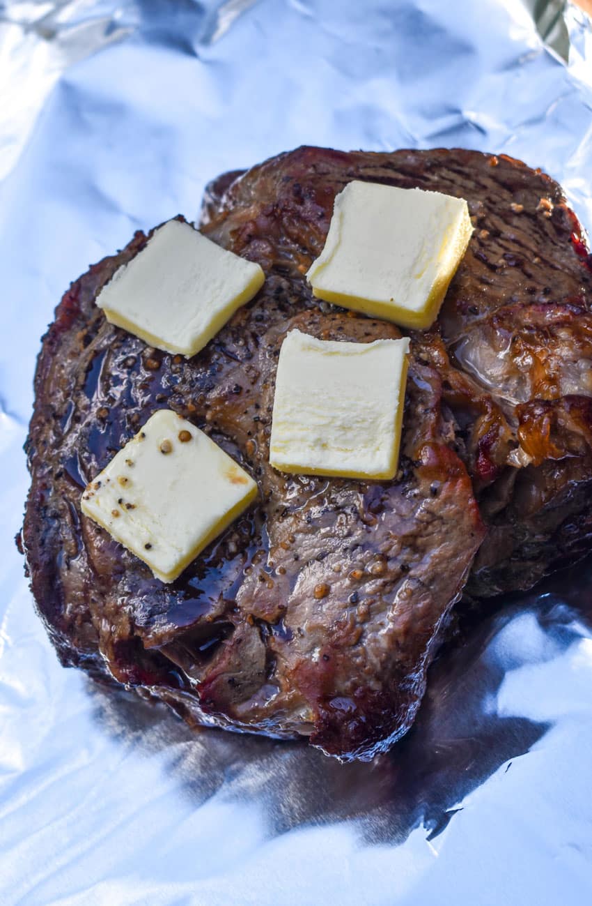 pats of butter on top of a smoked chuck roast resting on a sheet of aluminum foil