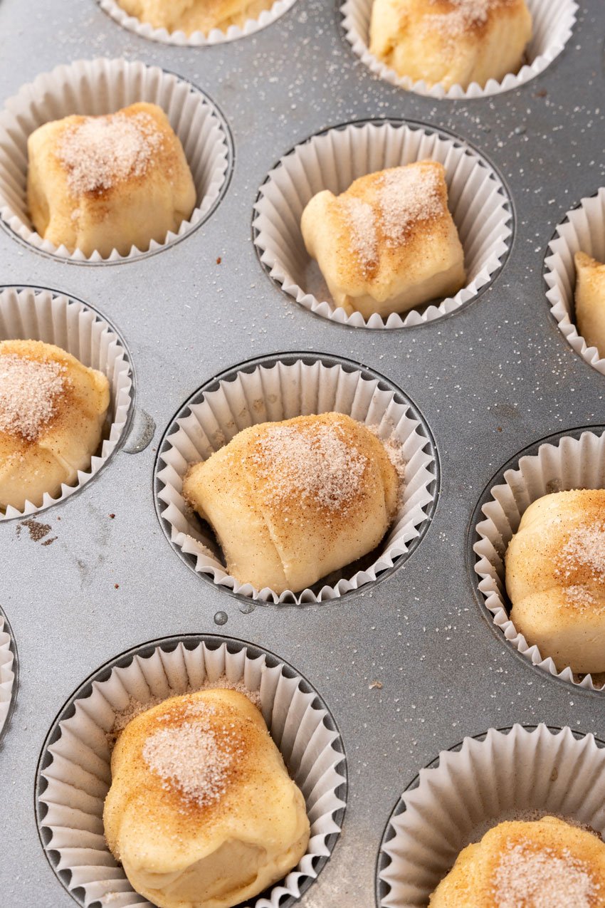 cinnamon sugar topped marshmallow stuffed crescent roll balls in a metal muffin tin pan