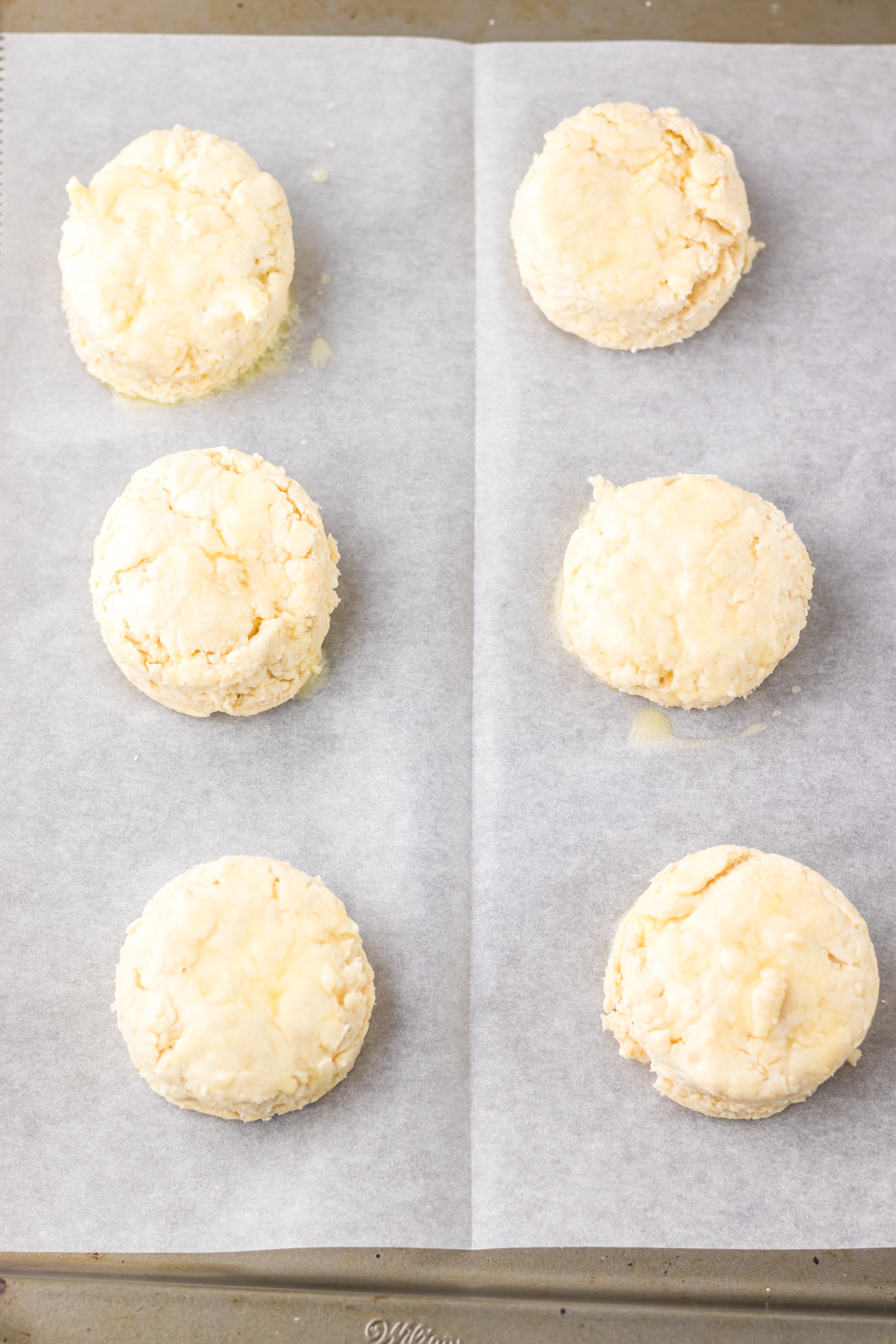unbaked homemade southern biscuits arranged in two rows on a parchment paper lined baking sheet