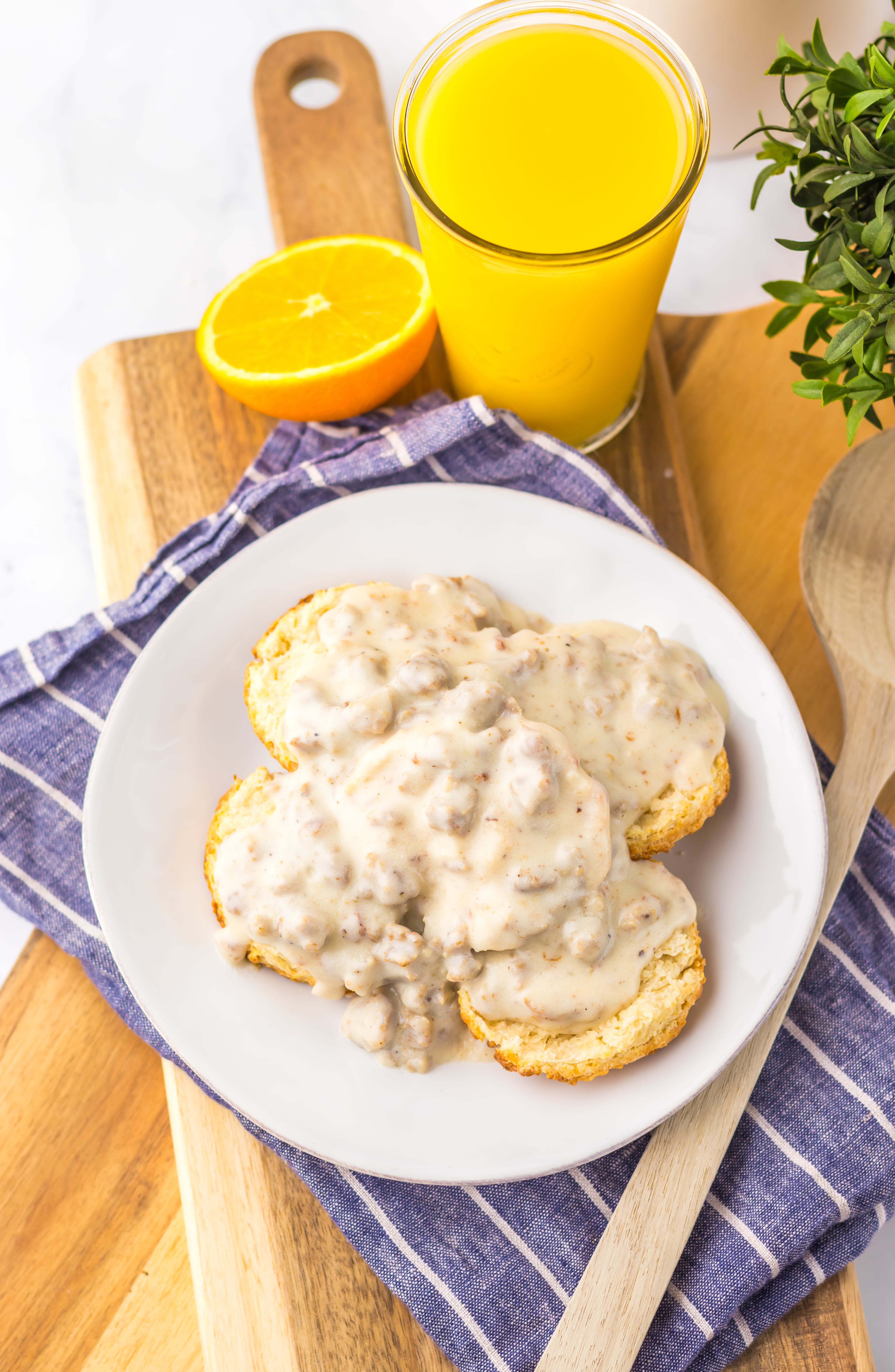 homemade sausage gravy over halved country biscuits on a white plate with a glass of orange juice in the background
