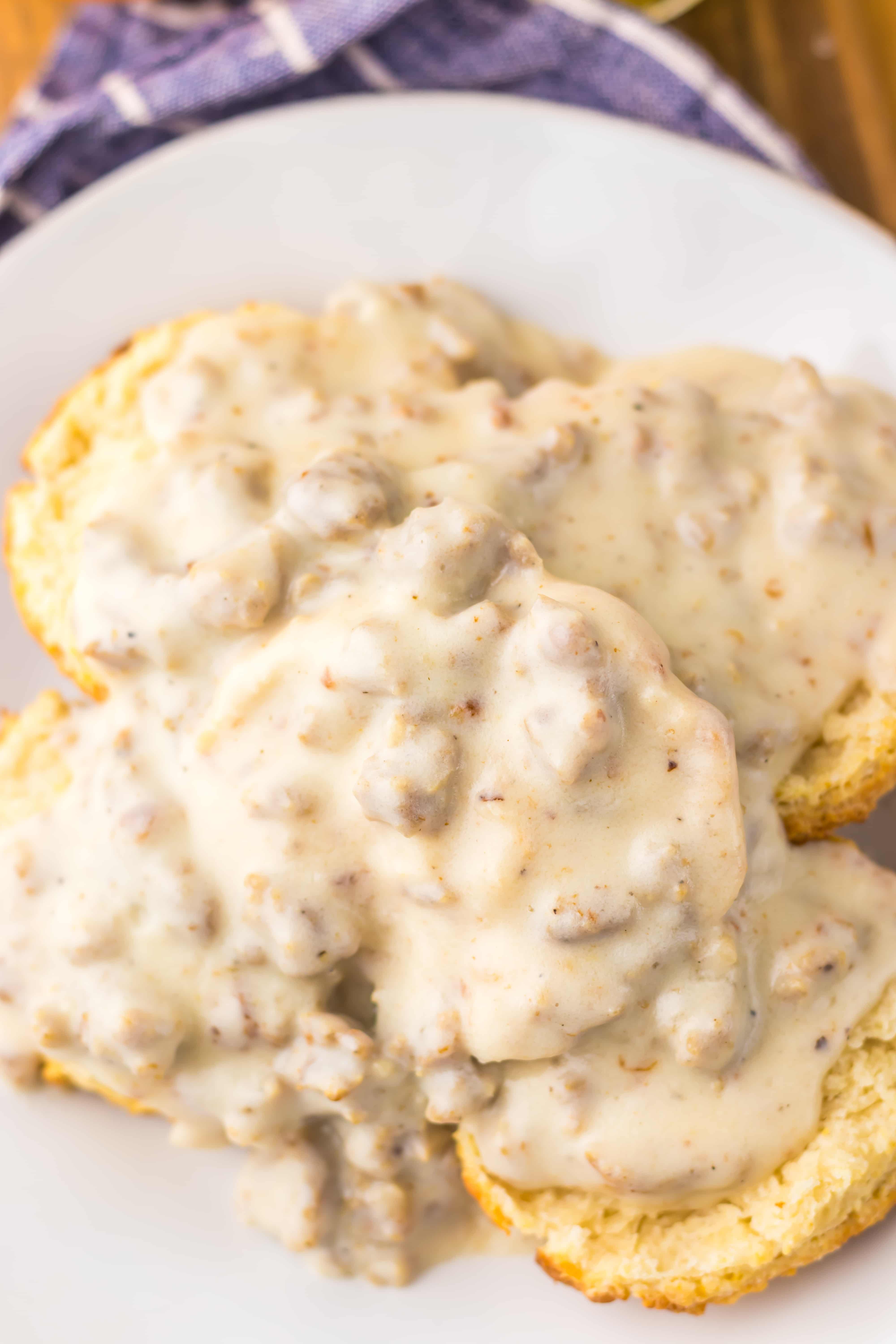 a close up of homemade sausage gravy over halved biscuits on a white plate