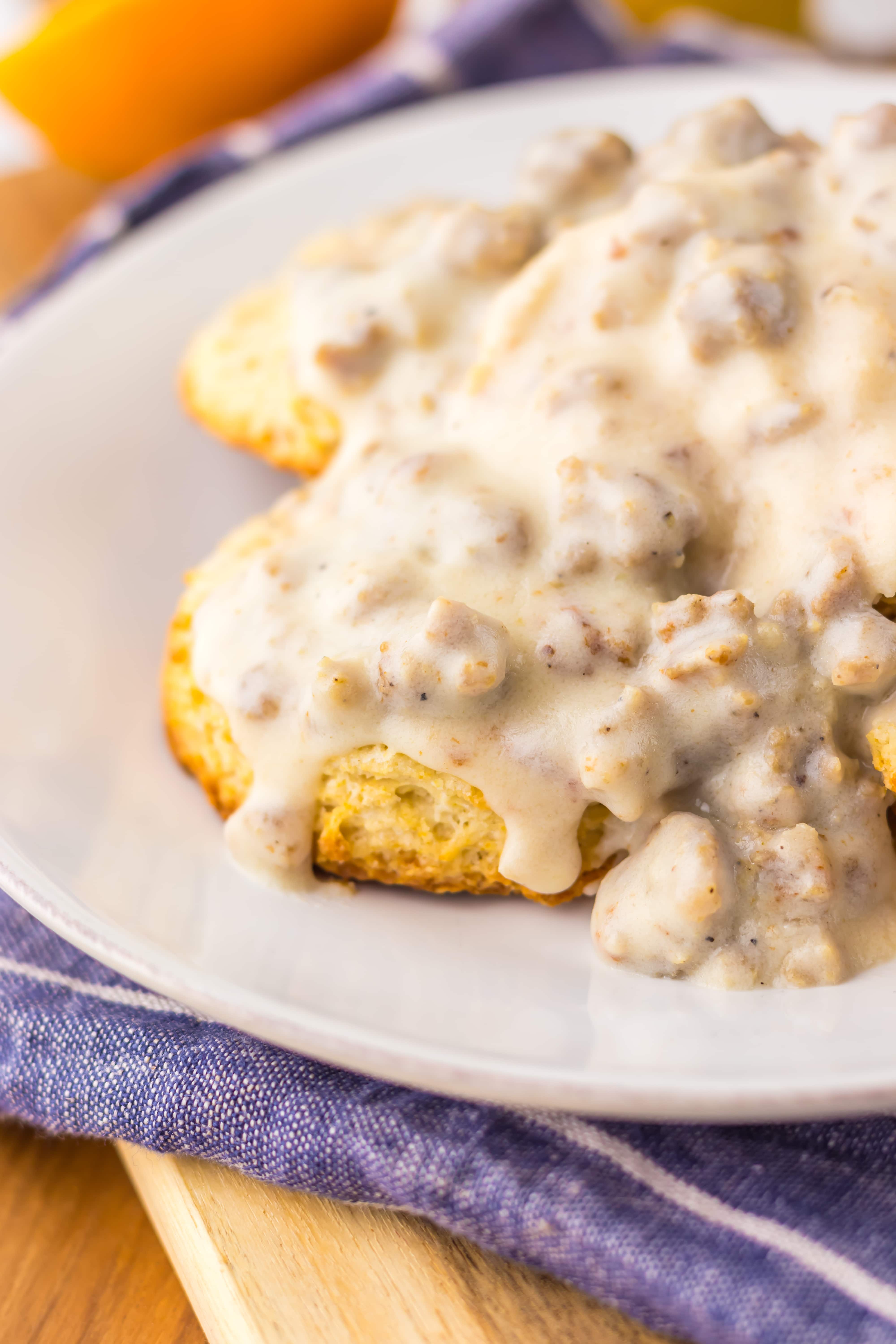 a close up of homemade sausage gravy over halved biscuits on a white plate
