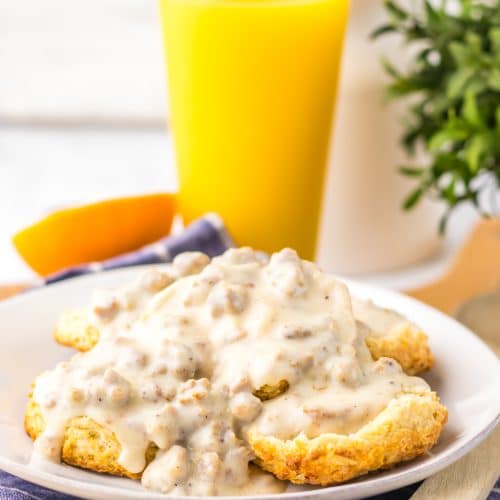 homemade sausage gravy over halved country biscuits on a white plate with a glass of orange juice in the background