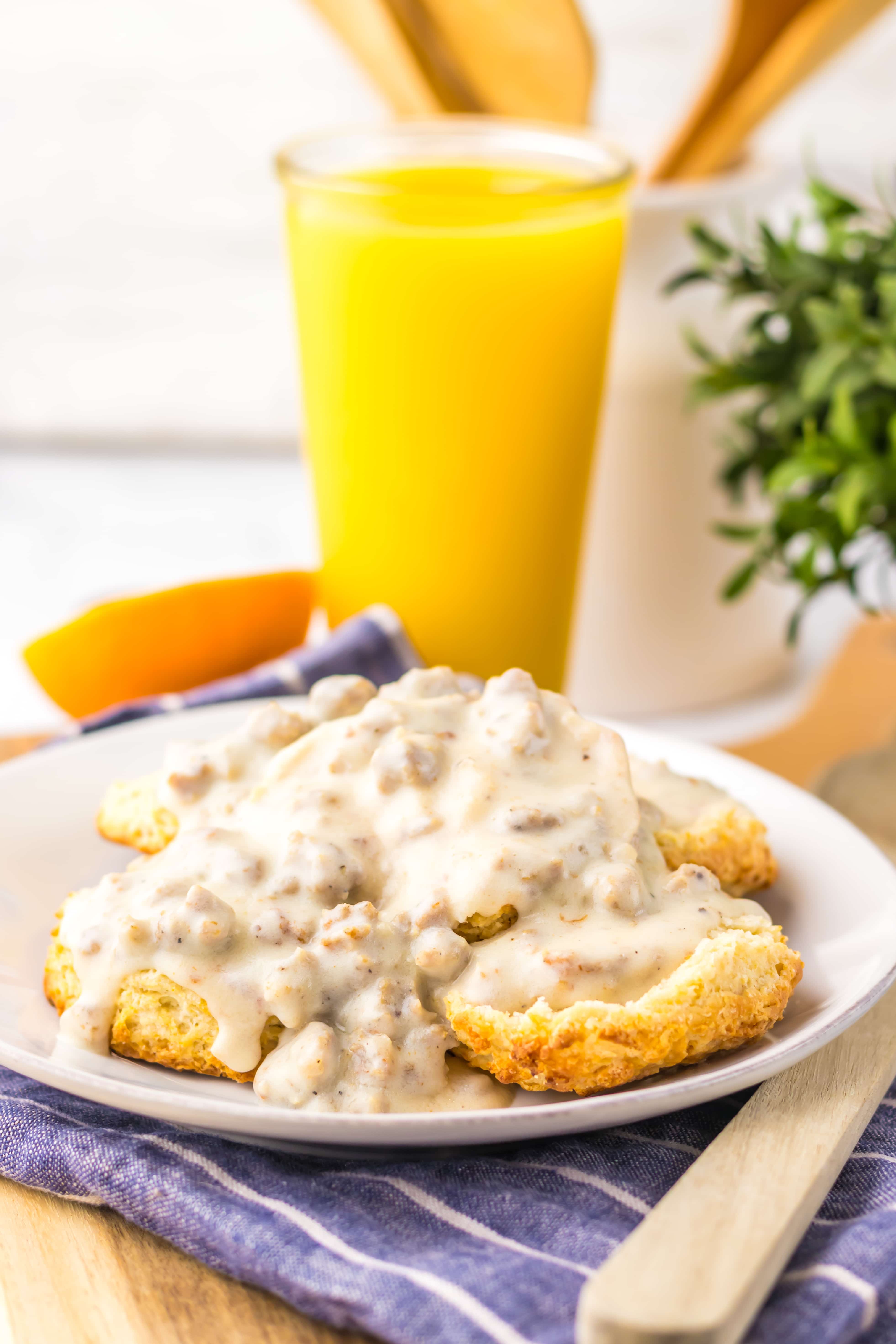 homemade sausage gravy over halved country biscuits on a white plate with a glass of orange juice in the background