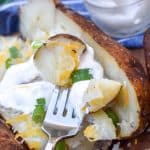 a silver fork scooping up a smoked baked potato chunk with sour cream and sliced green onions
