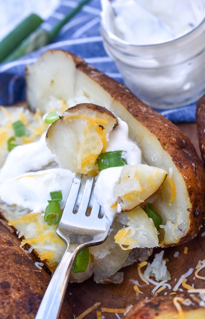 a silver fork scooping up a smoked baked potato chunk with sour cream and sliced green onions