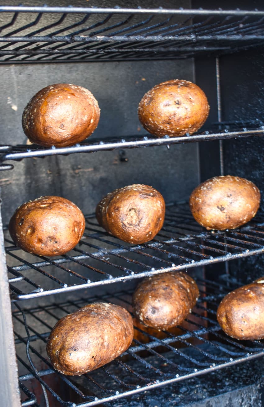 salted and oil rubbed large russet potatoes arranged in rows on the rack of an electric smoker