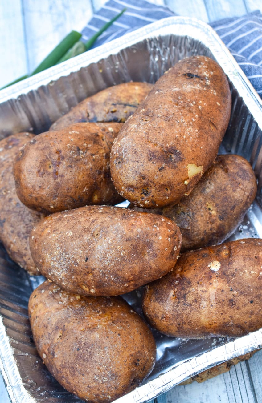 smoked baked potatoes piled in an aluminum foil pan