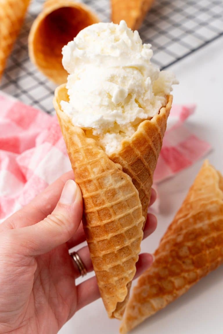 a hand holding up a homemade waffle cone filled with scoops of creamy vanilla ice cream