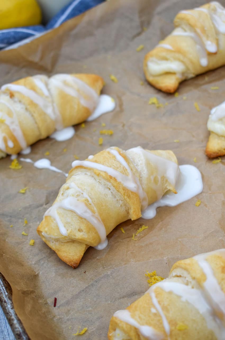 glazed lemon crescent rolls arranged in rows on a parchment paper lined baking sheet