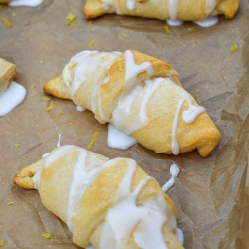 glazed lemon crescent rolls arranged in rows on a parchment paper lined baking sheet