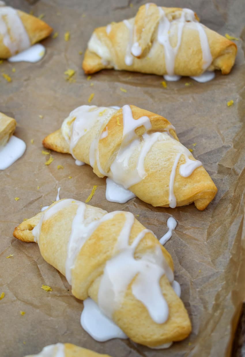 glazed lemon crescent rolls arranged in rows on a parchment paper lined baking sheet