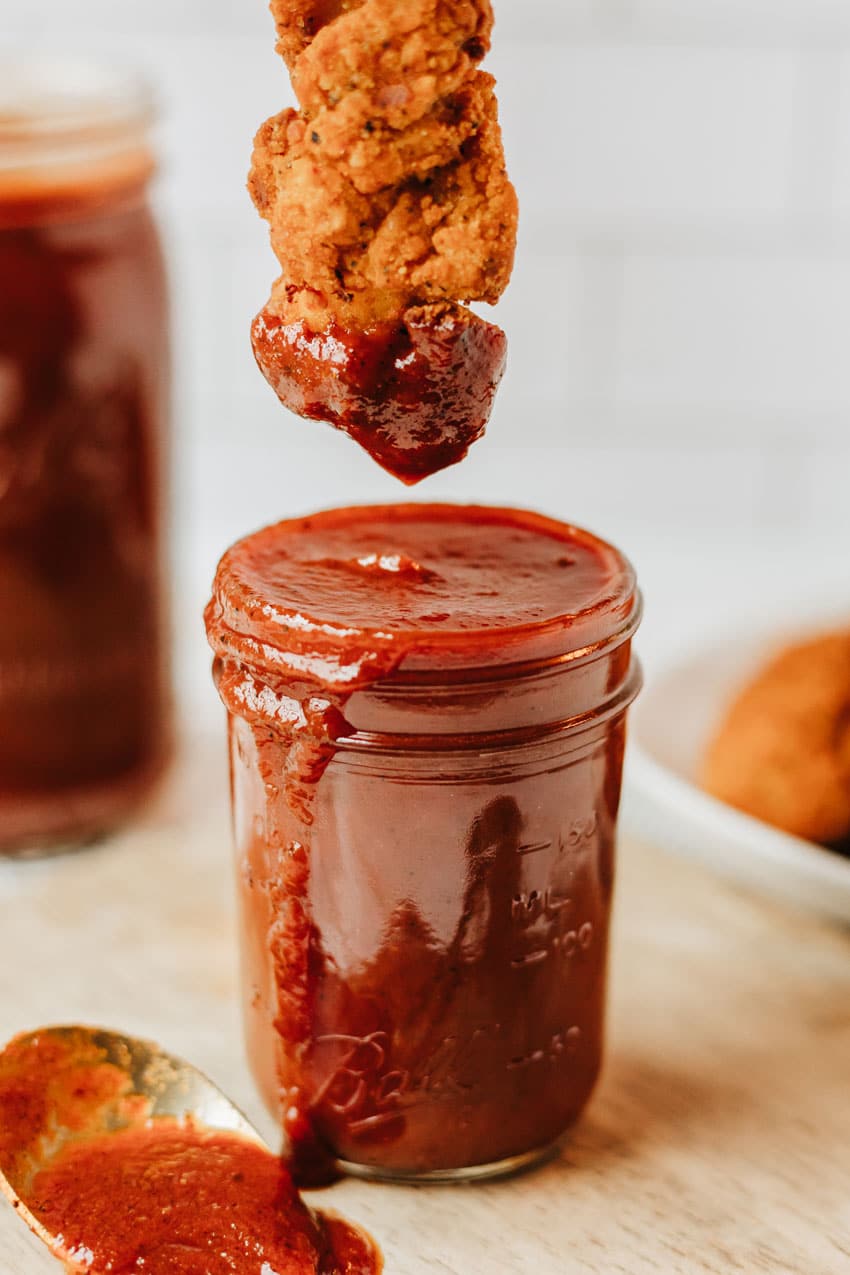 a crispy chicken tender being dipping in a jar of homemade barbecue sauce