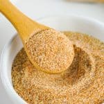a wooden spoon scooping homemade seasoning salt out of a small white bowl