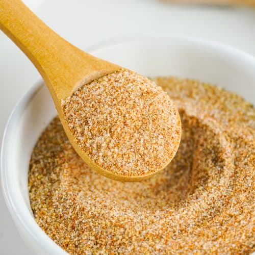 a wooden spoon scooping homemade seasoning salt out of a small white bowl