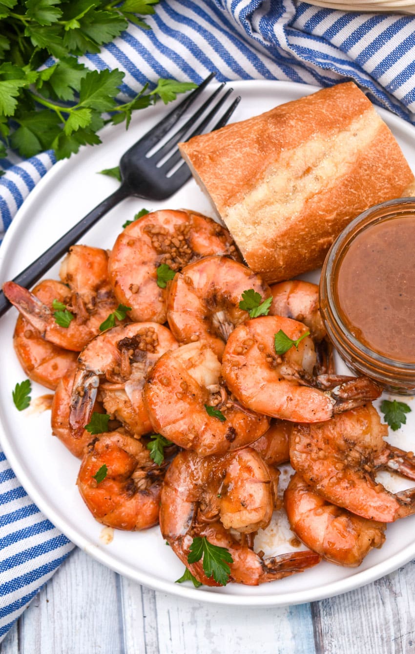 new orleans barbecue shrimp on a white plate with a slice of bread and a small bowl of sauce on the side