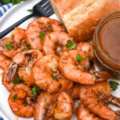 new orleans barbecue shrimp on a white plate with a slice of bread and a small bowl of sauce on the side