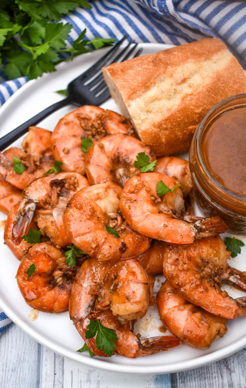 new orleans barbecue shrimp on a white plate with a slice of bread and a small bowl of sauce on the side