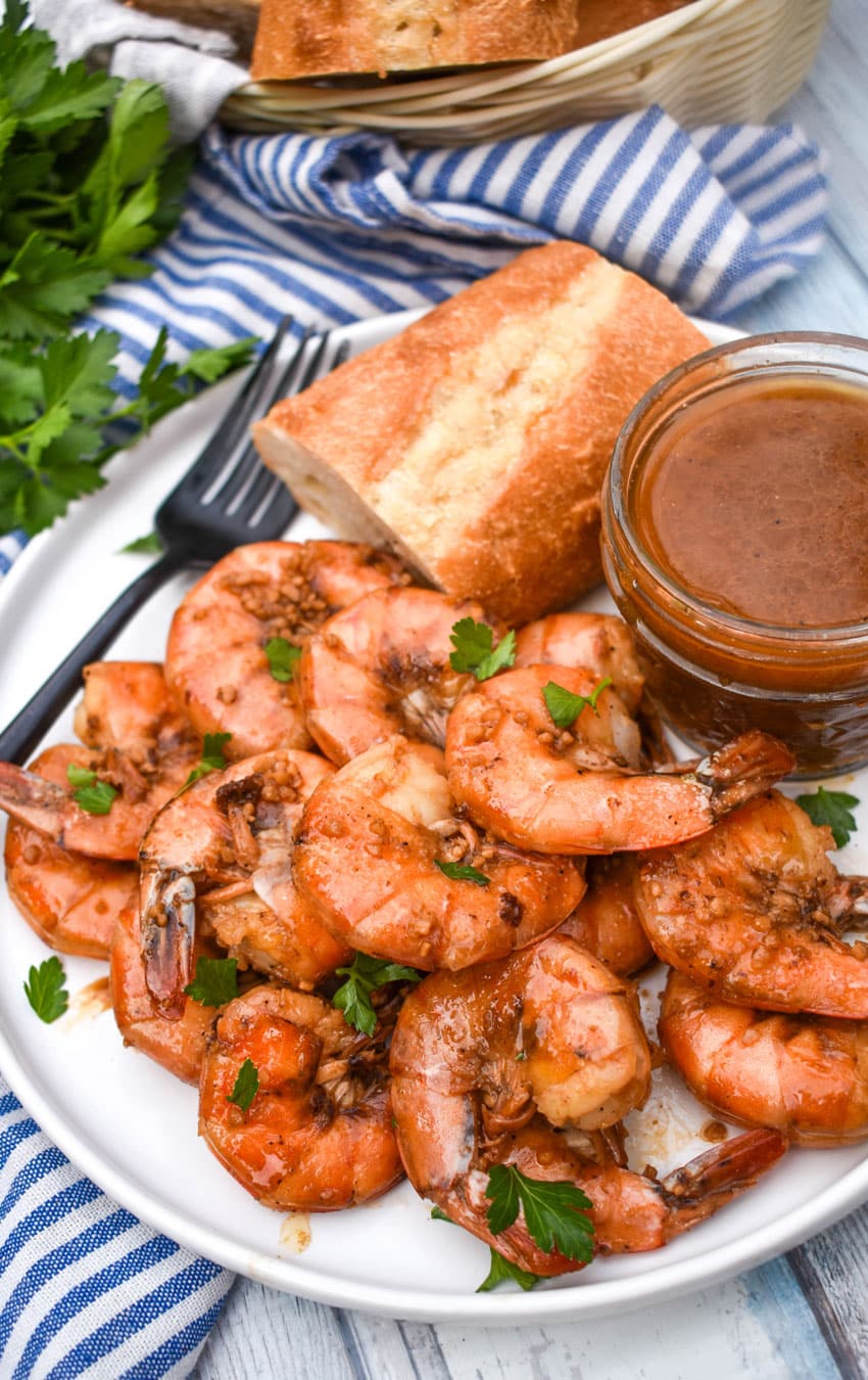 new orleans barbecue shrimp on a white plate with a slice of bread and a small bowl of sauce on the side