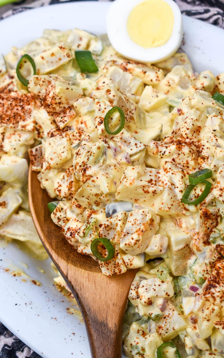 a wooden spoon scooping smoked potato salad out of a white bowl