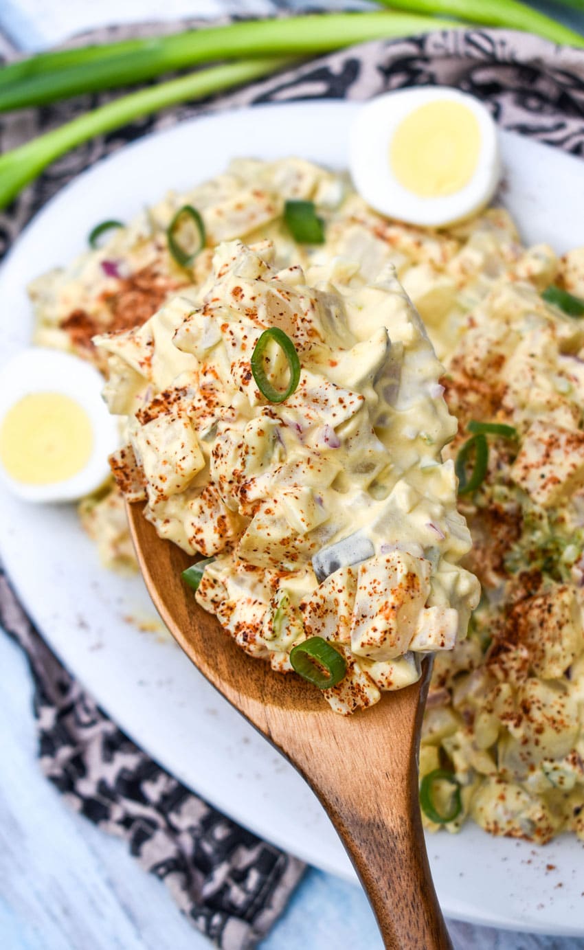 a wooden spoon holding up a scoop of smoked potato salad