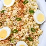 smoked potato salad topped with hard boiled egg halves in a white serving dish