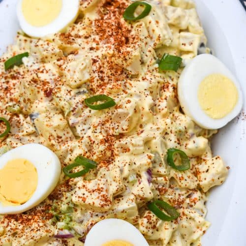 smoked potato salad topped with hard boiled egg halves in a white serving dish