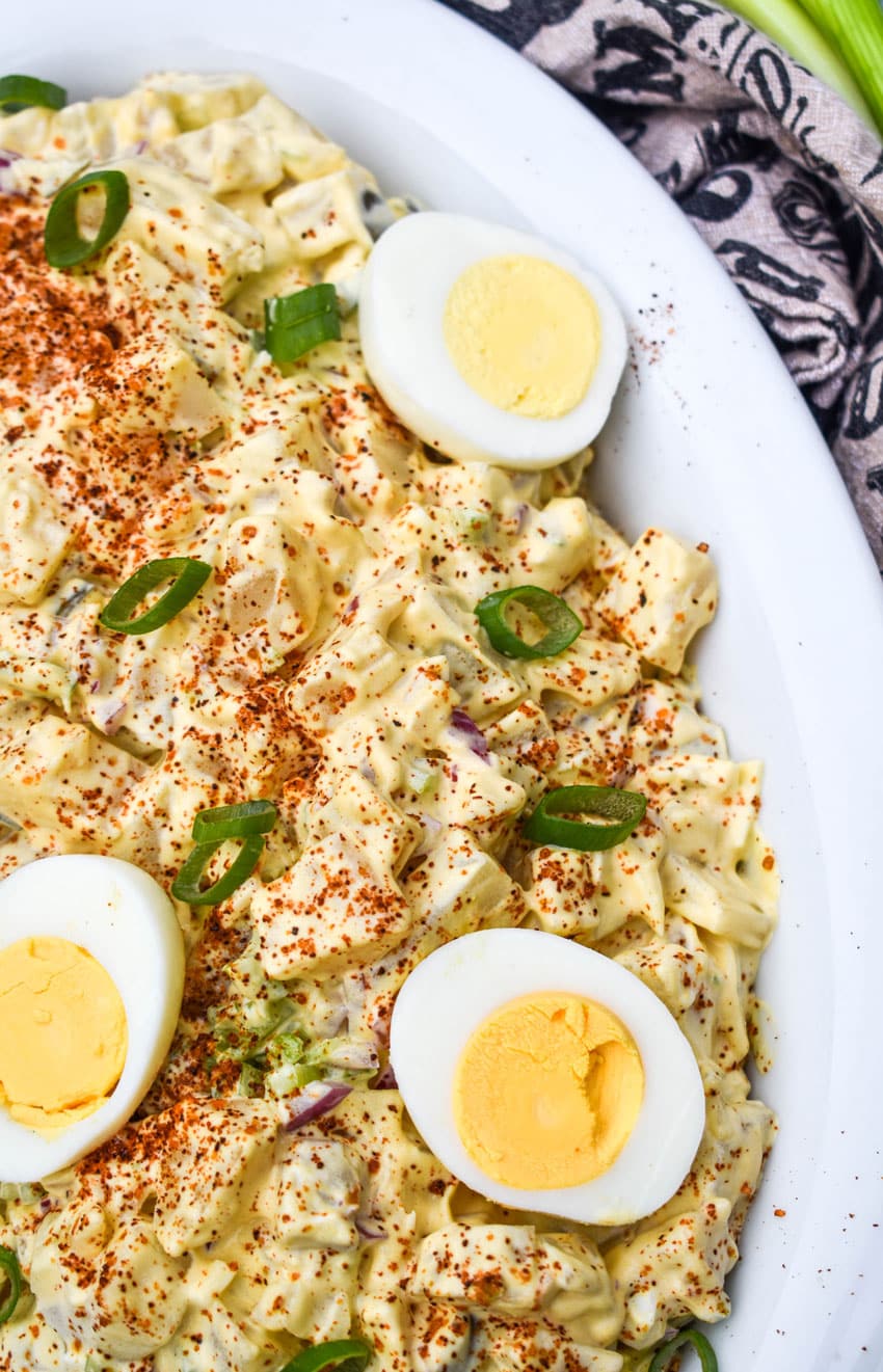 smoked potato salad topped with hard boiled egg halves in a white serving dish