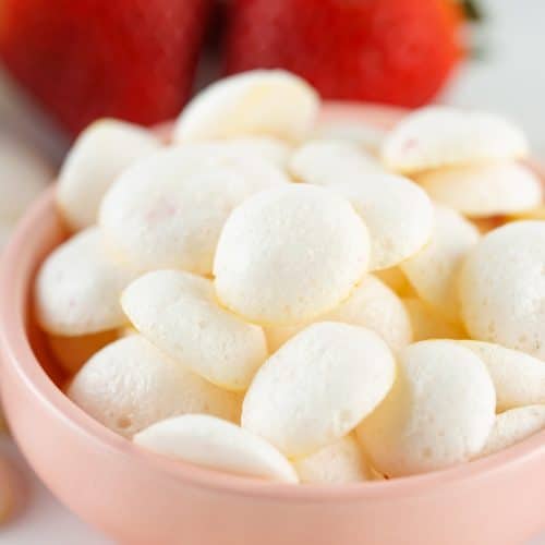 homemade yogurt melts piled in a small pink bowl with fresh strawberries in the background