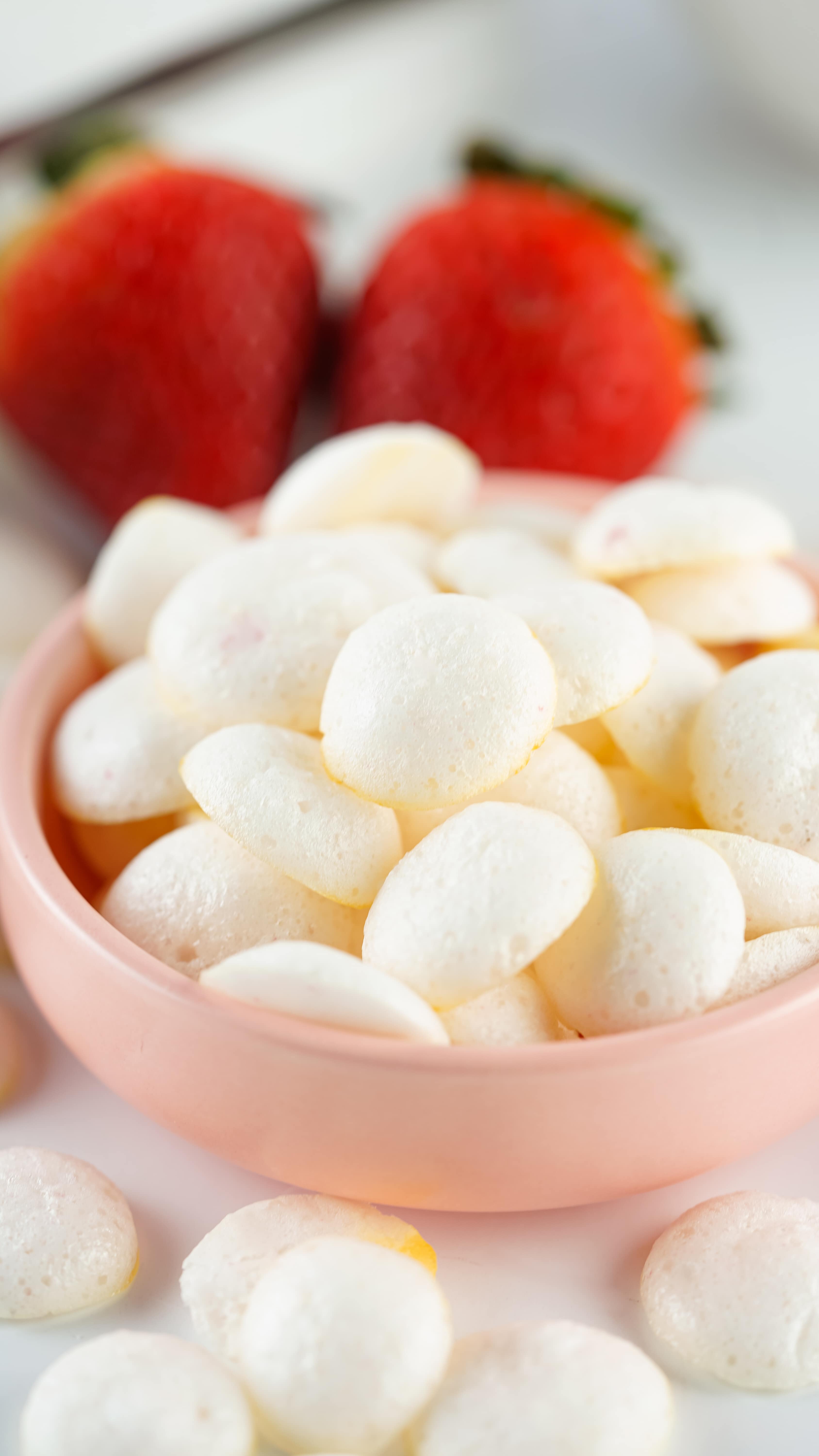 homemade yogurt melts piled in a small pink bowl with fresh strawberries in the background