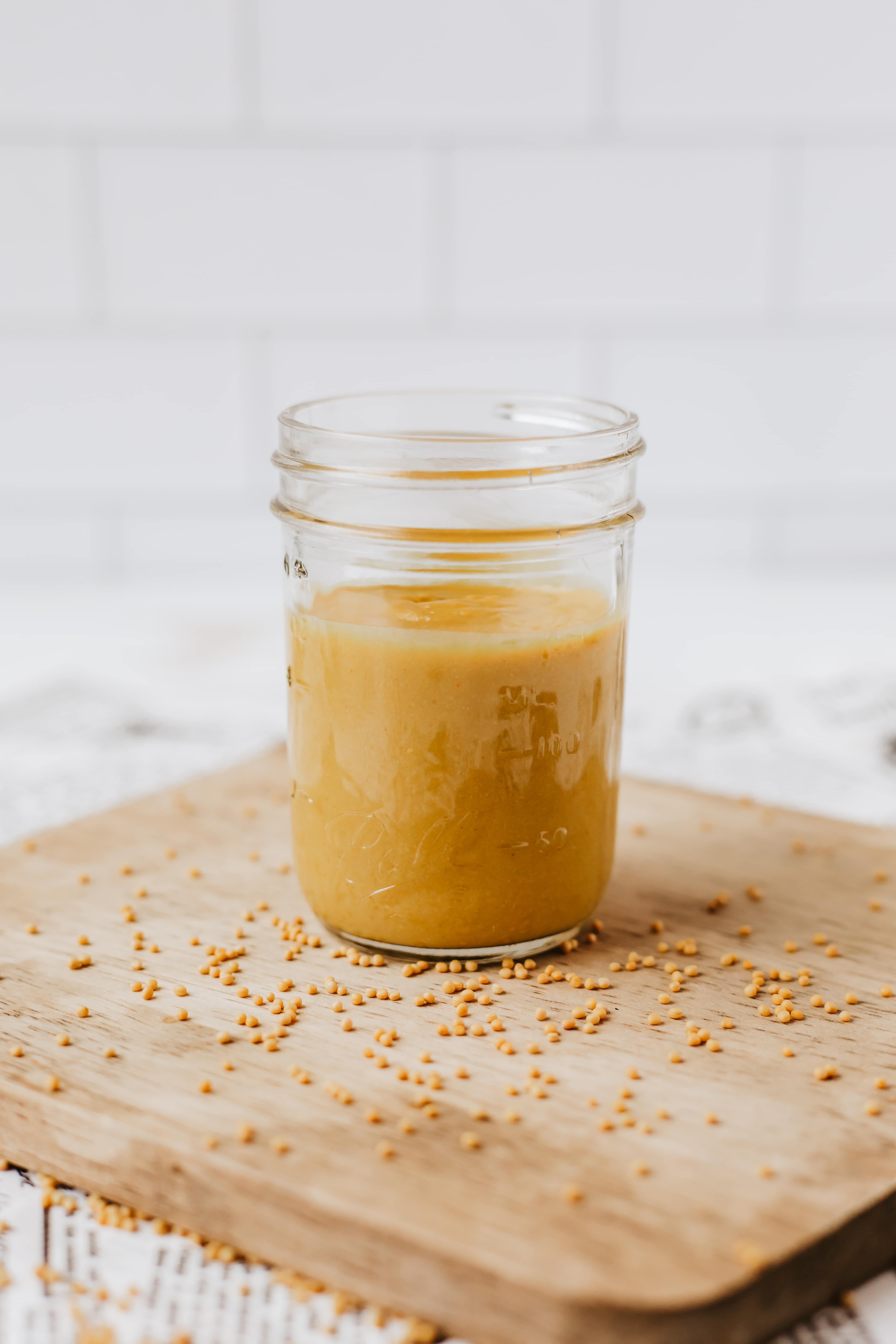 homemade yellow mustard in a small glass jar sitting on a wooden cutting board