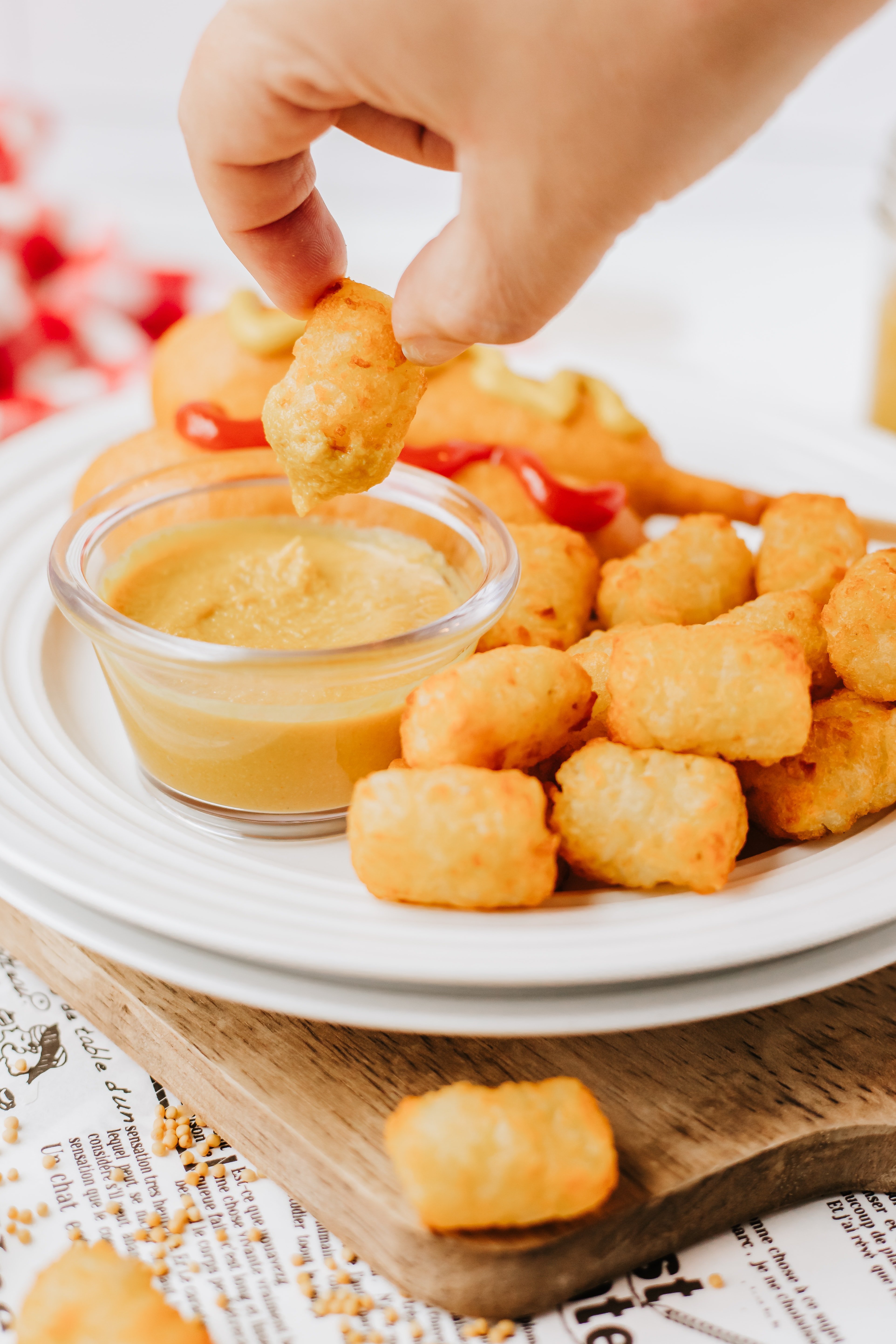 a hand holding up a crispy tater tot dipped in homemade yellow mustard