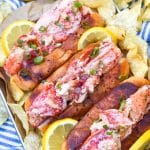three homemade lobster rolls on a metal serving pan with potato chips on the sides